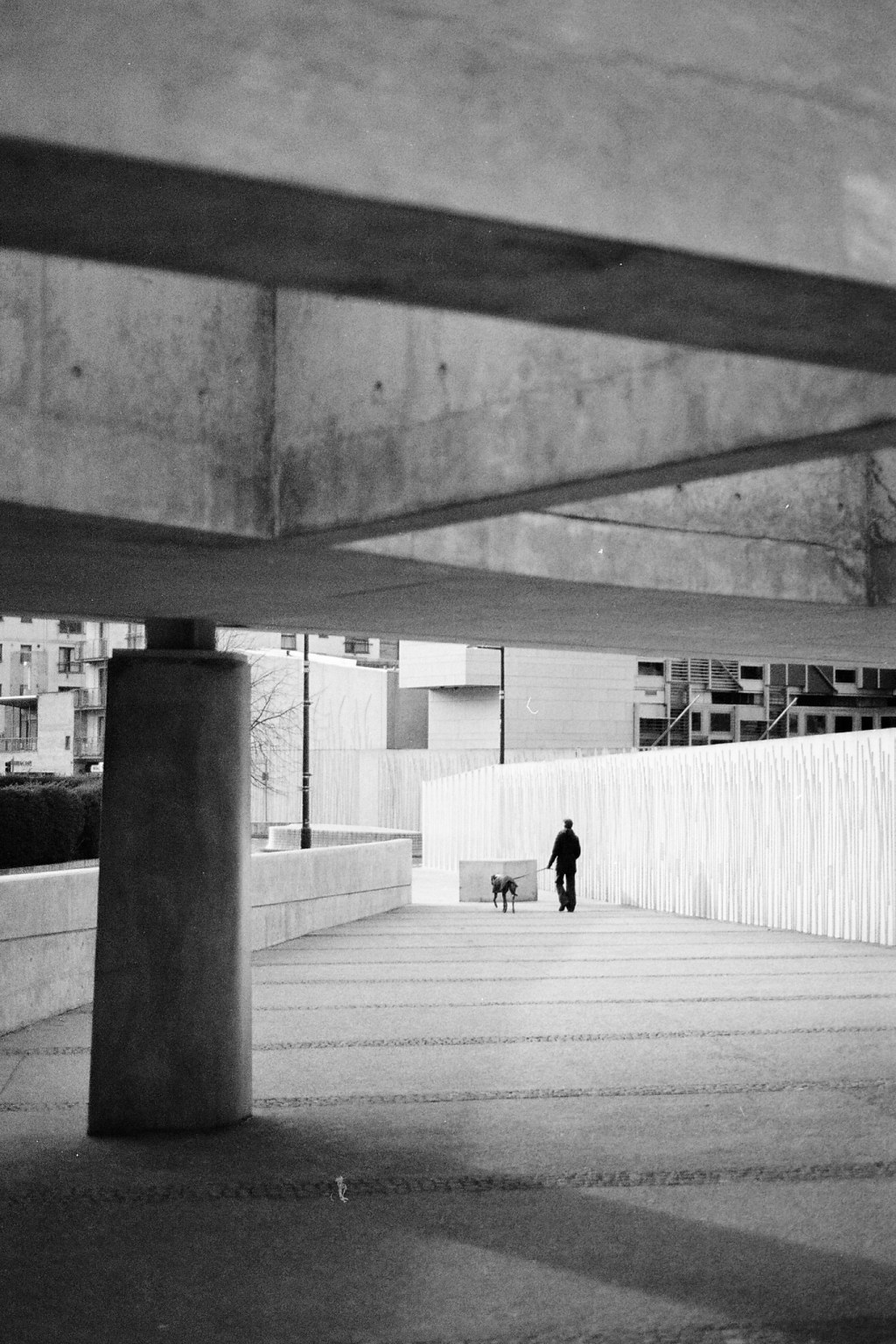 Black and white. A lone figure on a wide concrete ramp, framed by heavy beams.