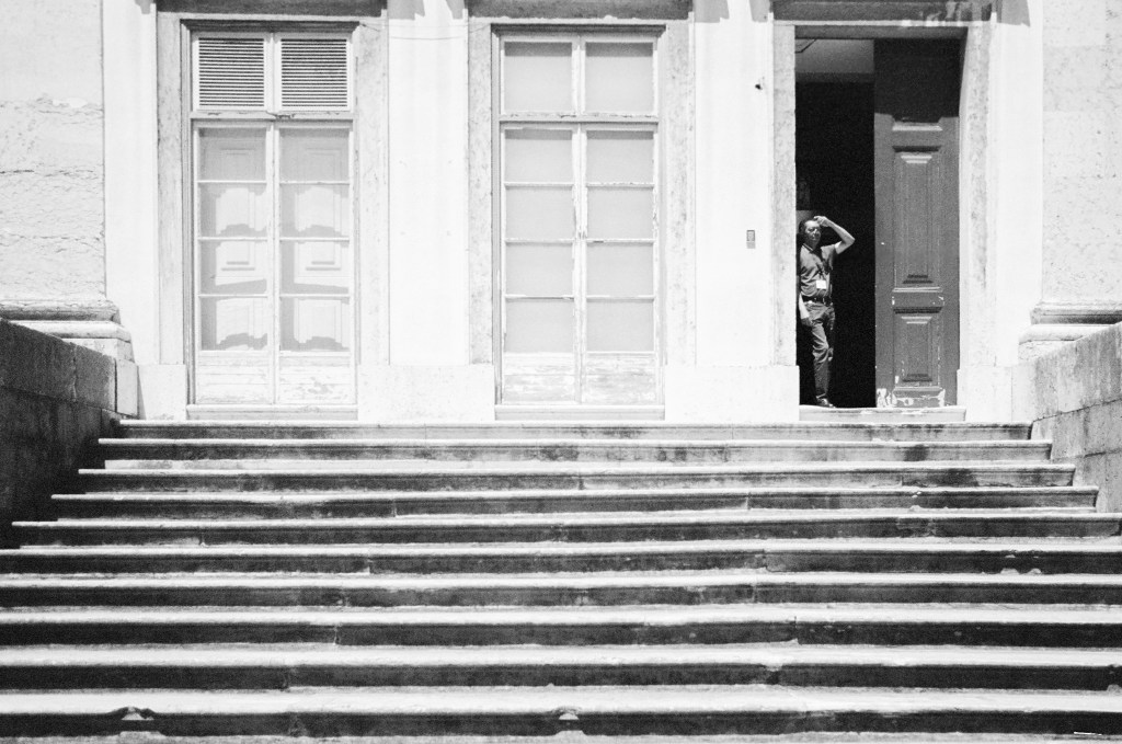 Black and white. A person standing in a doorway at the top of a flight of stone steps.