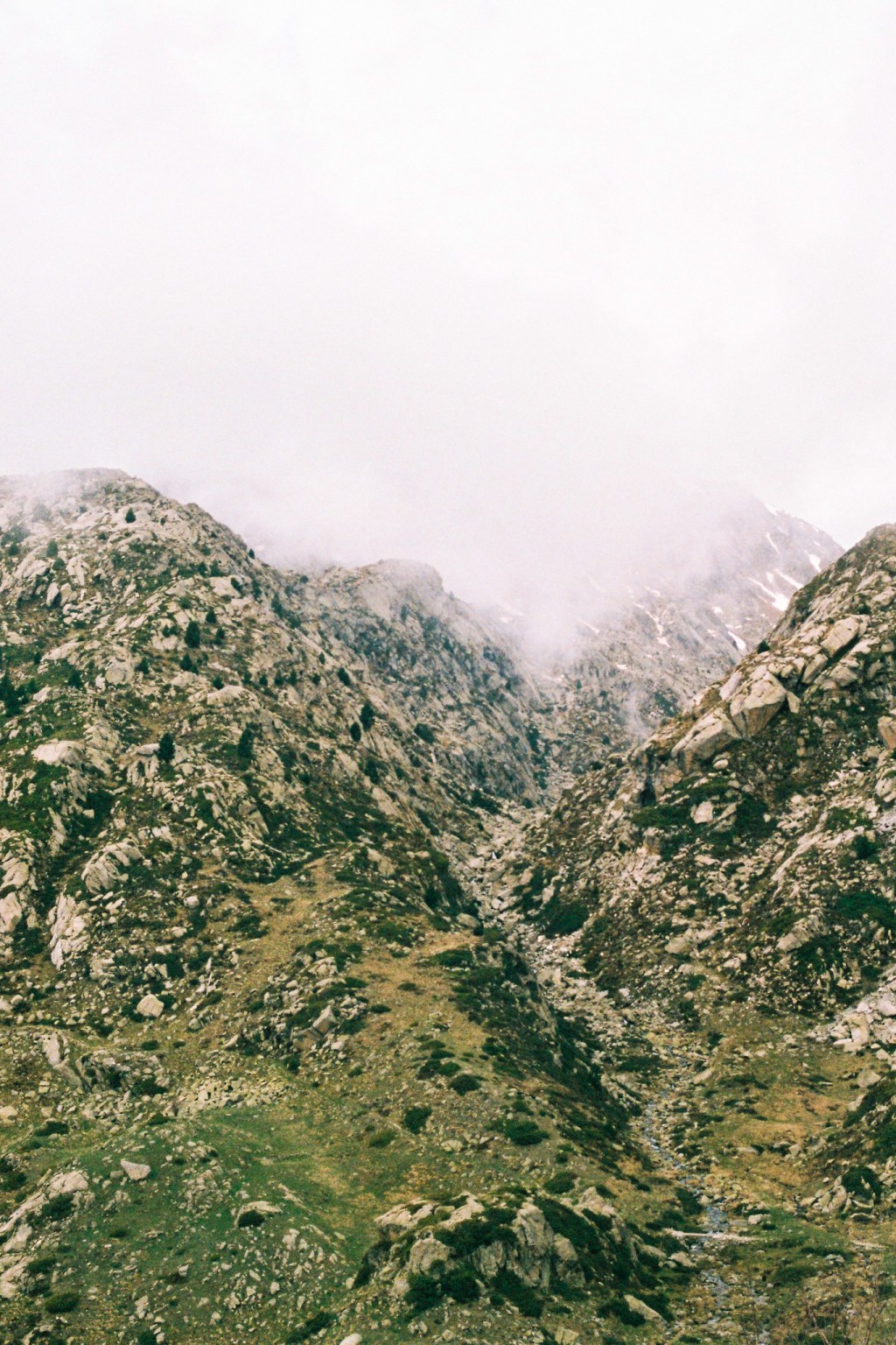 A green, rock-strewn valley rising into white cloud.