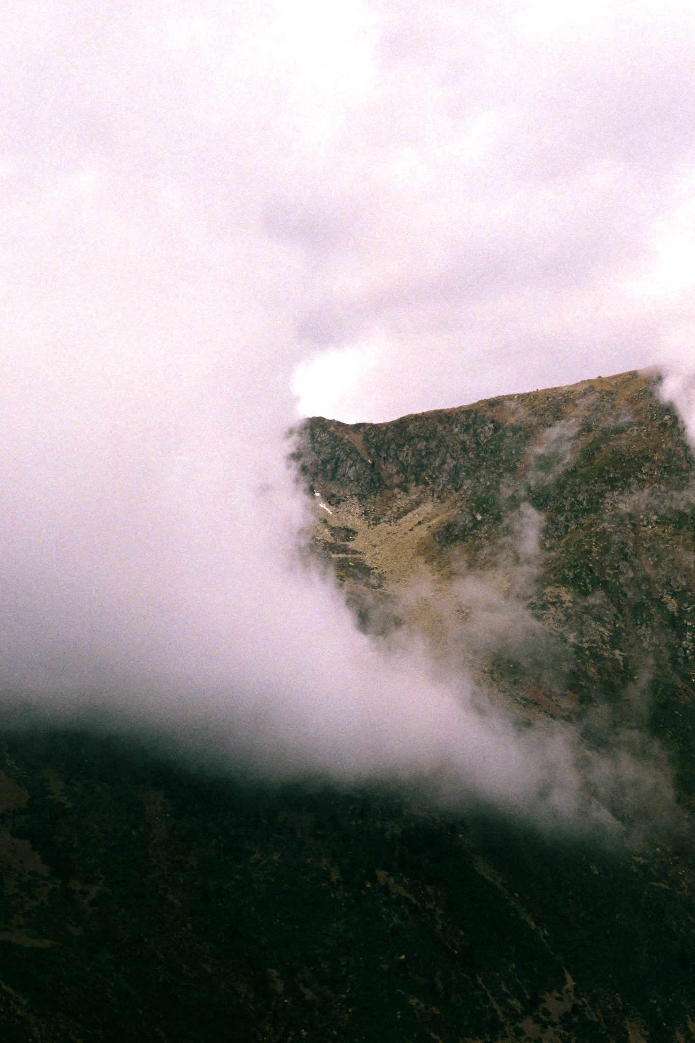 Pale pink cloud spilling down a steep green mountainside.