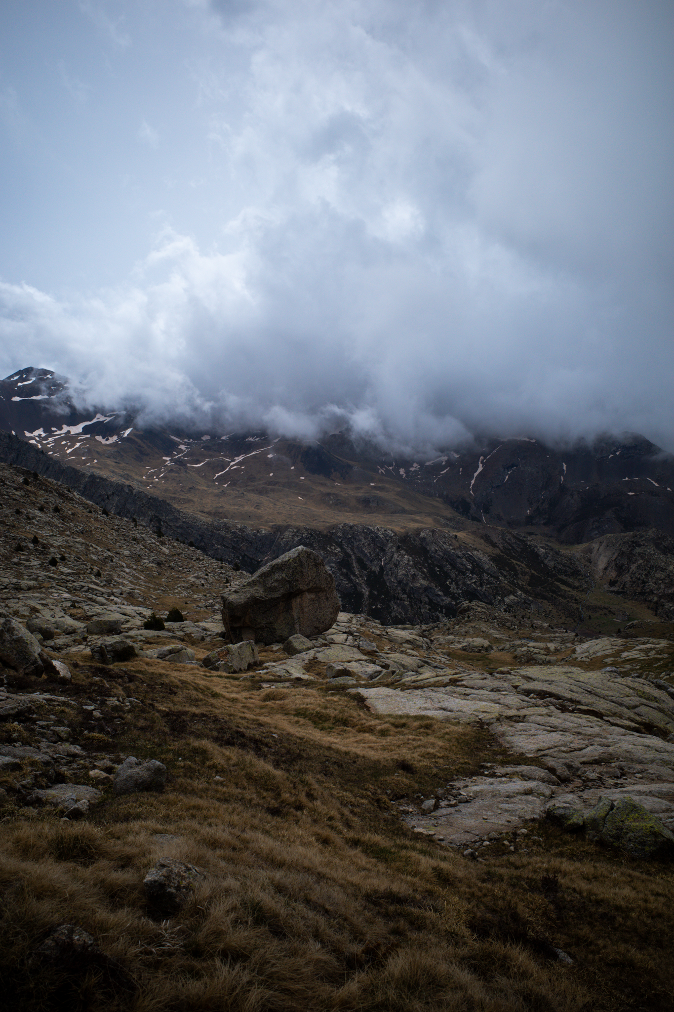 Low cloud covering a mountain ridge above a boulder-strewn slope of brown grass.