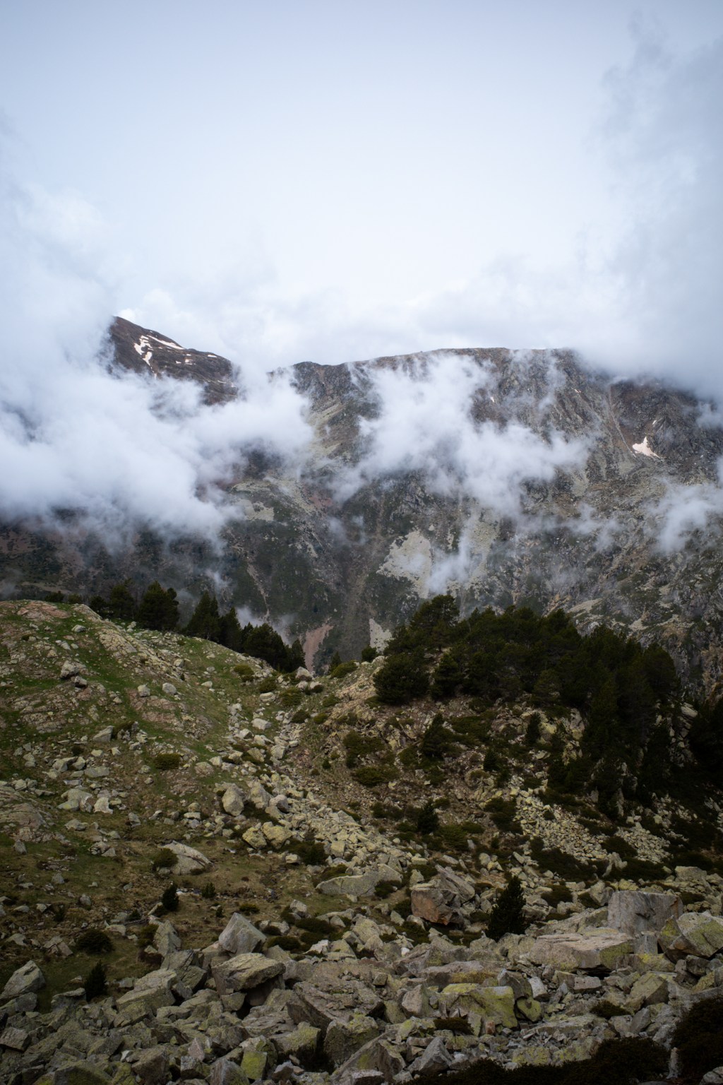 Cloud pouring over a rocky ridge, with scree and dark pines below.