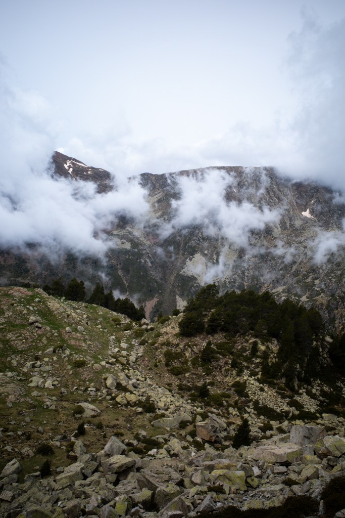 Cloud pouring over a rocky ridge, with scree and dark pines below.