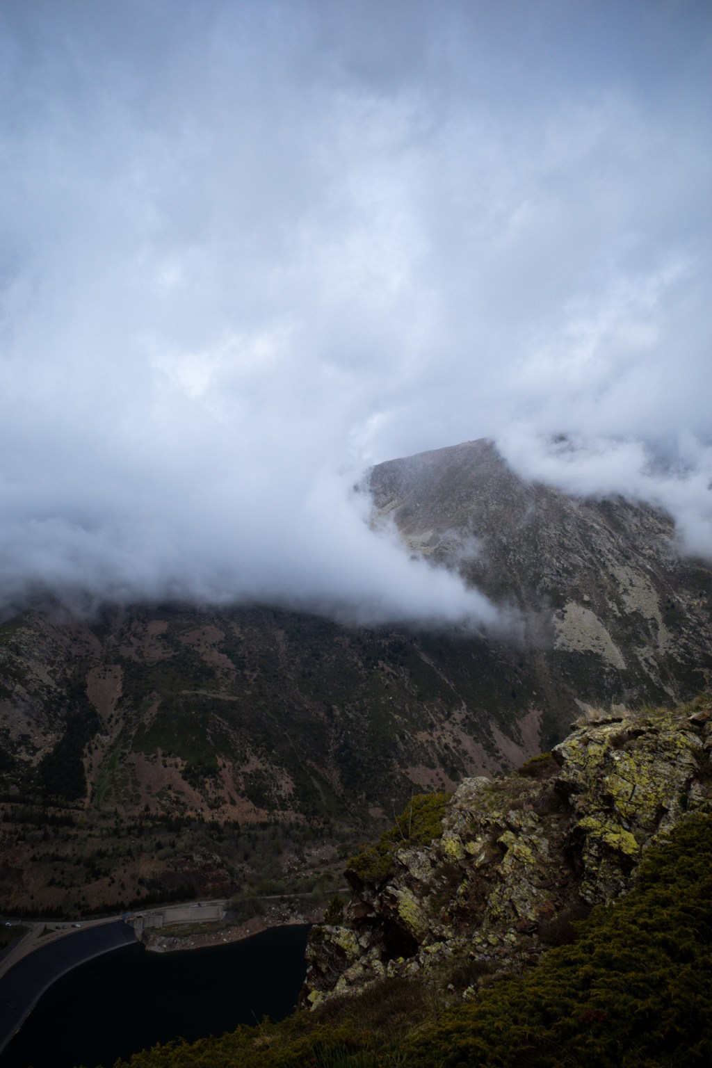 Heavy cloud sitting on a dark peak, with the edge of a reservoir below.