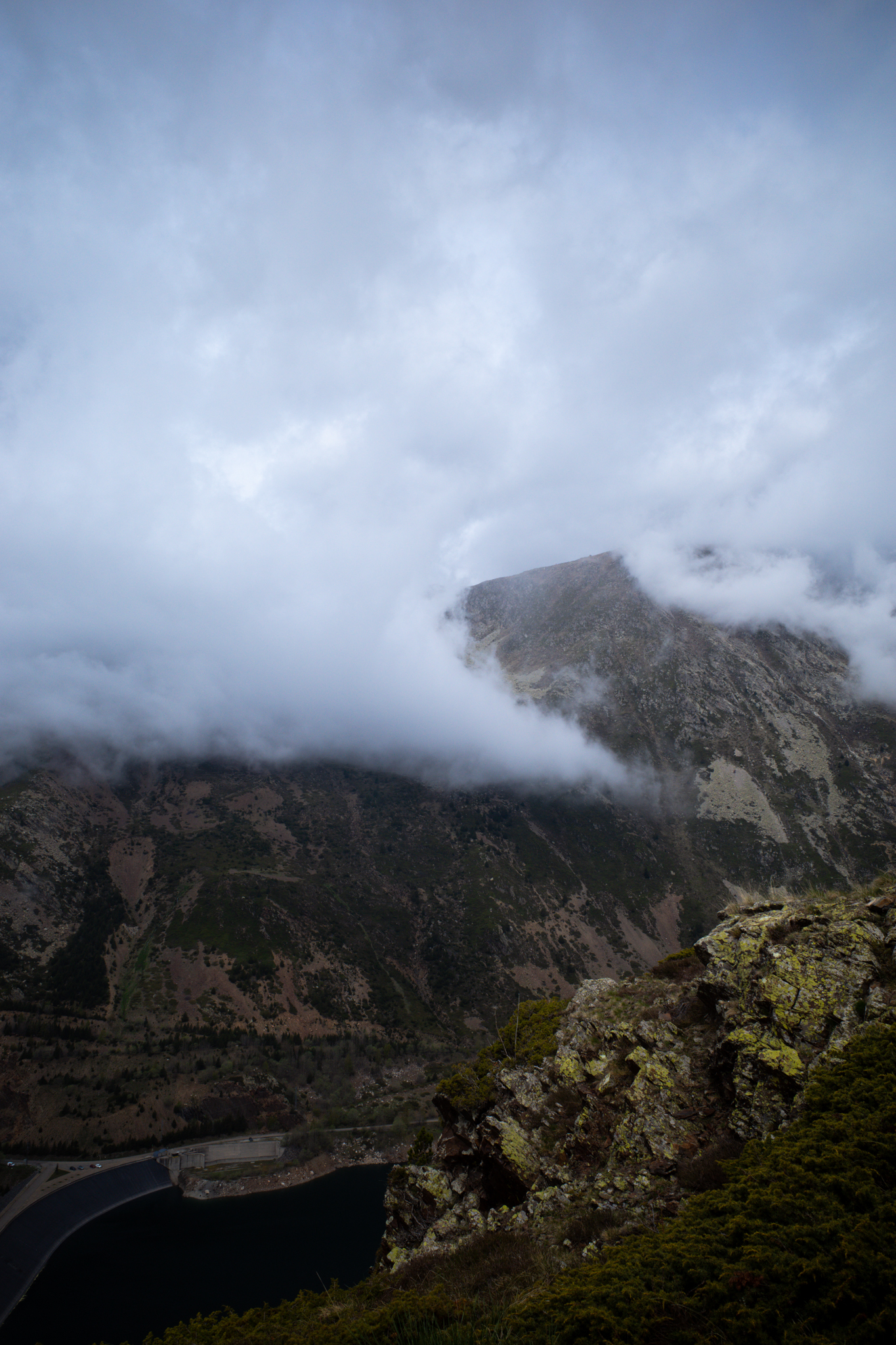 Heavy cloud sitting on a dark peak, with the edge of a reservoir below.