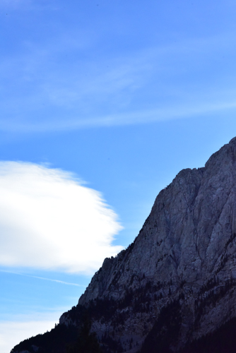 A lens-shaped white cloud beside a dark rock face under a blue sky.